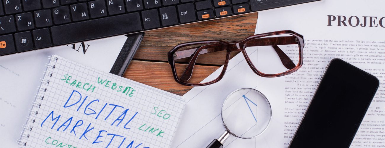 Digital marketing on notepad and various business papers on brown background. Digital marketing on notepad and various business papers on brown background. Brown glasses magnifier and smartphone near notepad.